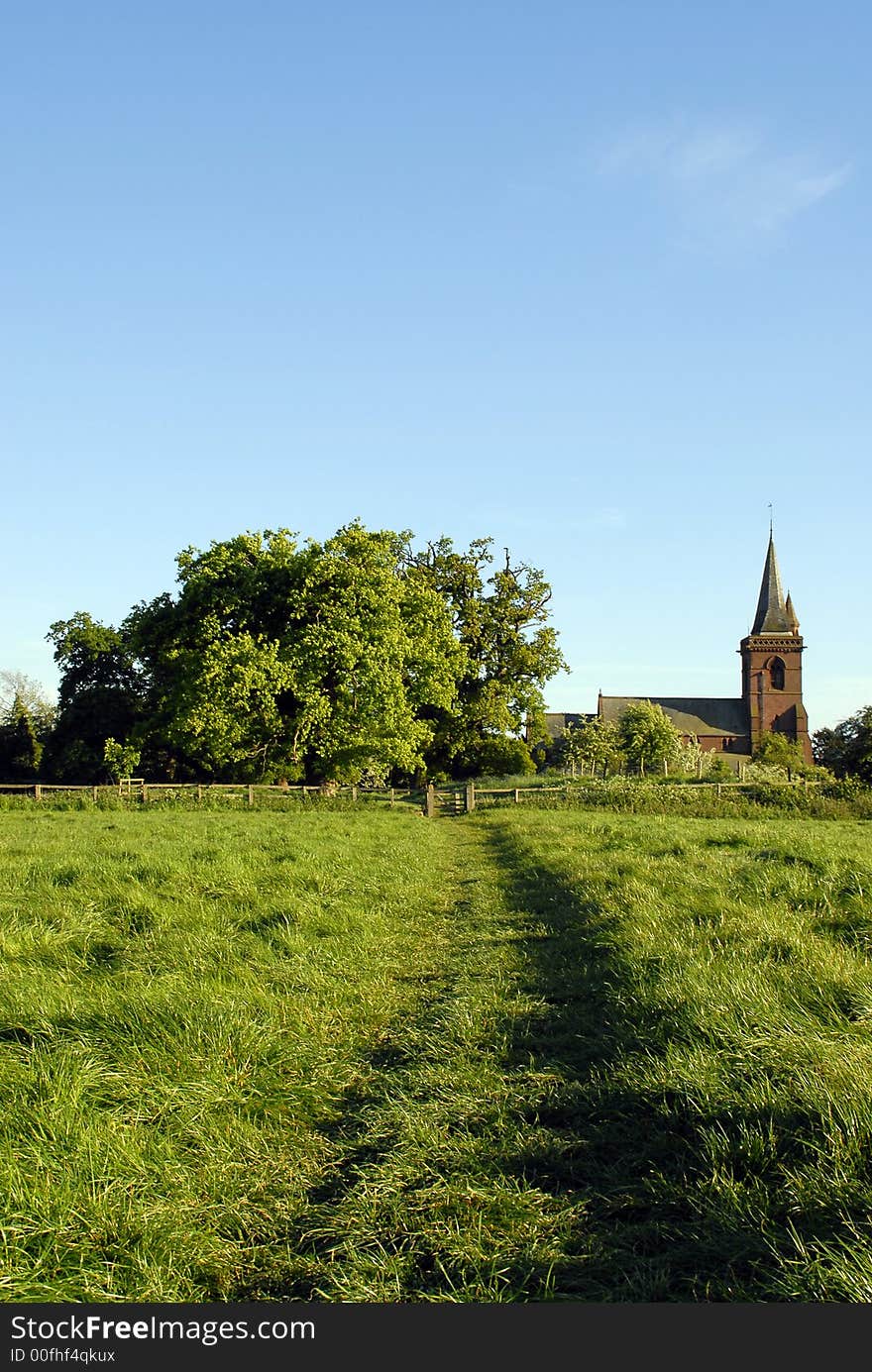 Rural parish church framed between old oak trees at the end of a footpath through a field.Portrait View