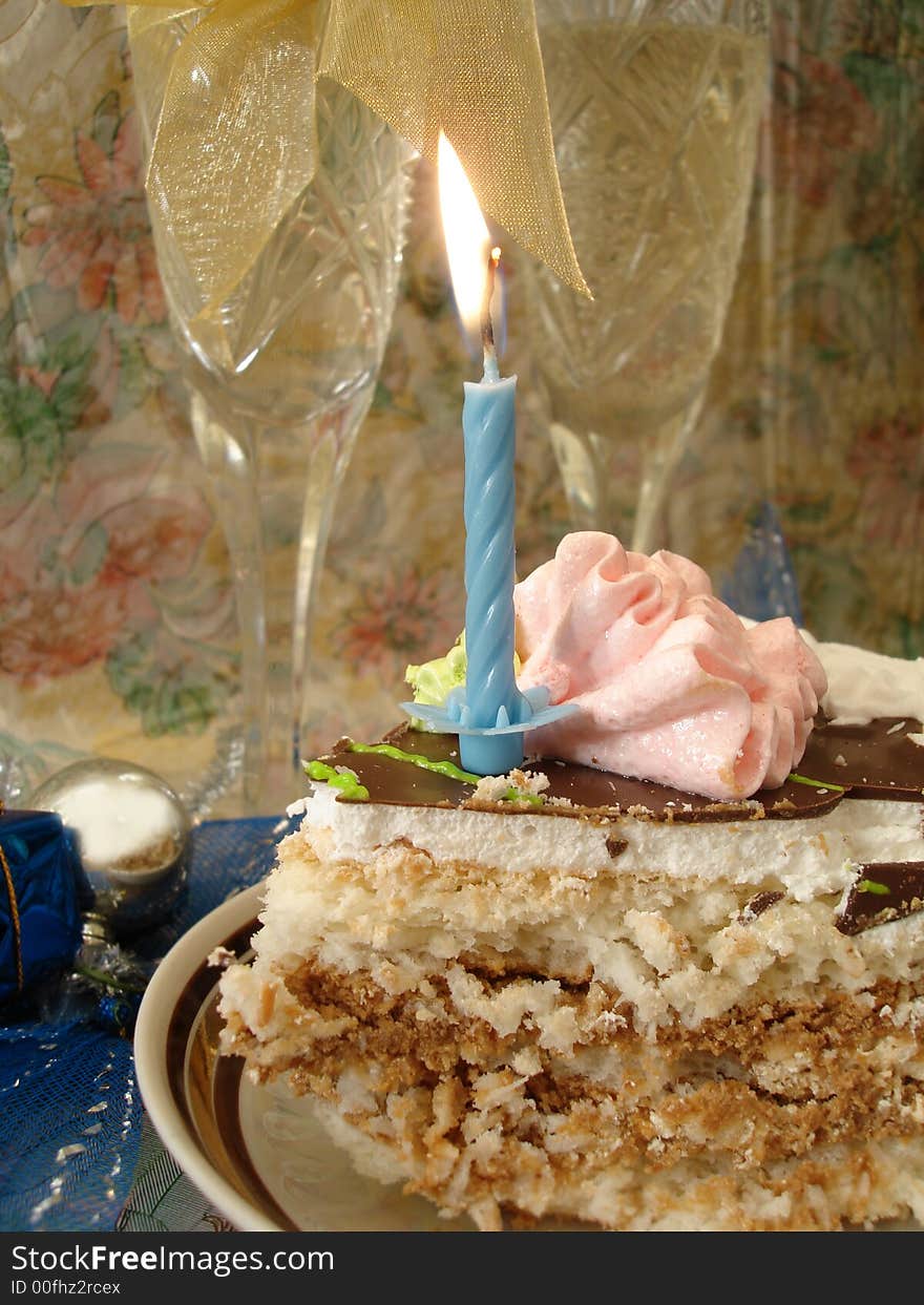 Celebratory table (piece of birthday cake and blue candle, two glasses with champagne)