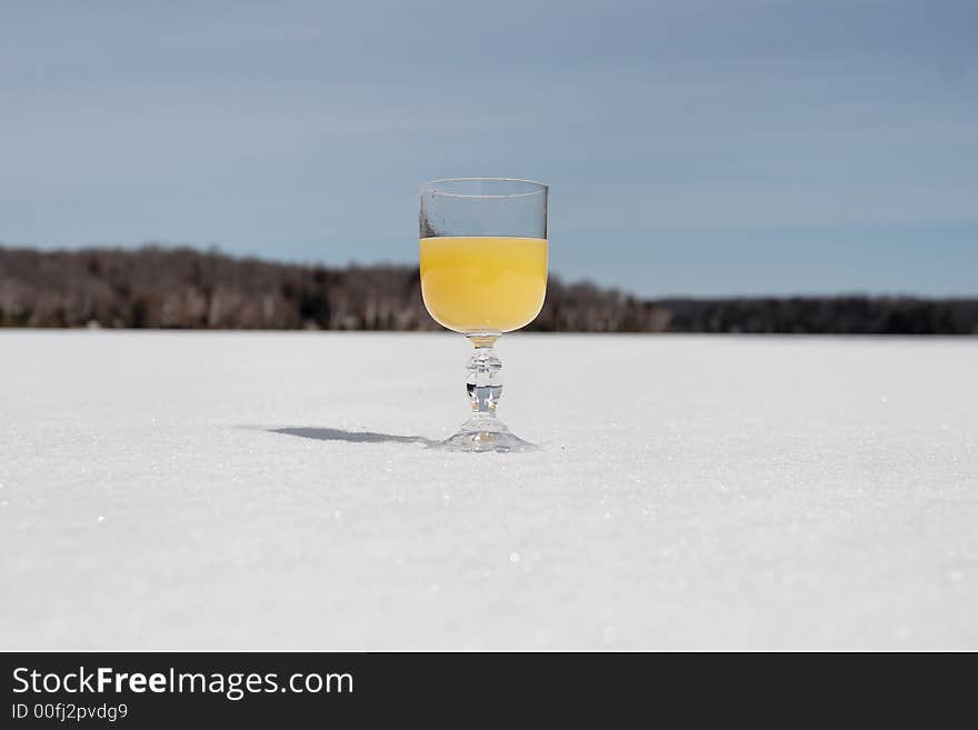 A glass of orange colored drink stands on a frozen lake. A glass of orange colored drink stands on a frozen lake