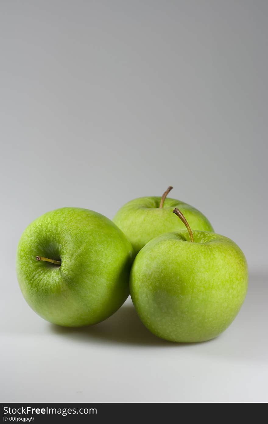 Three tasty green apples on grey background. Copyspace provided.