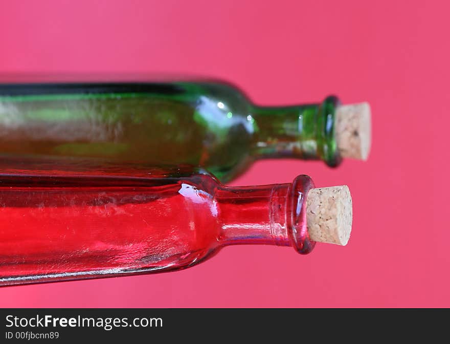 Emtpy red and green glass bottles with corks in the tops. Shot against a red background