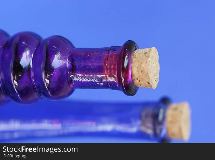 Empty blue and purple glass bottle with corks in the tops. Shot against a blue background. Empty blue and purple glass bottle with corks in the tops. Shot against a blue background