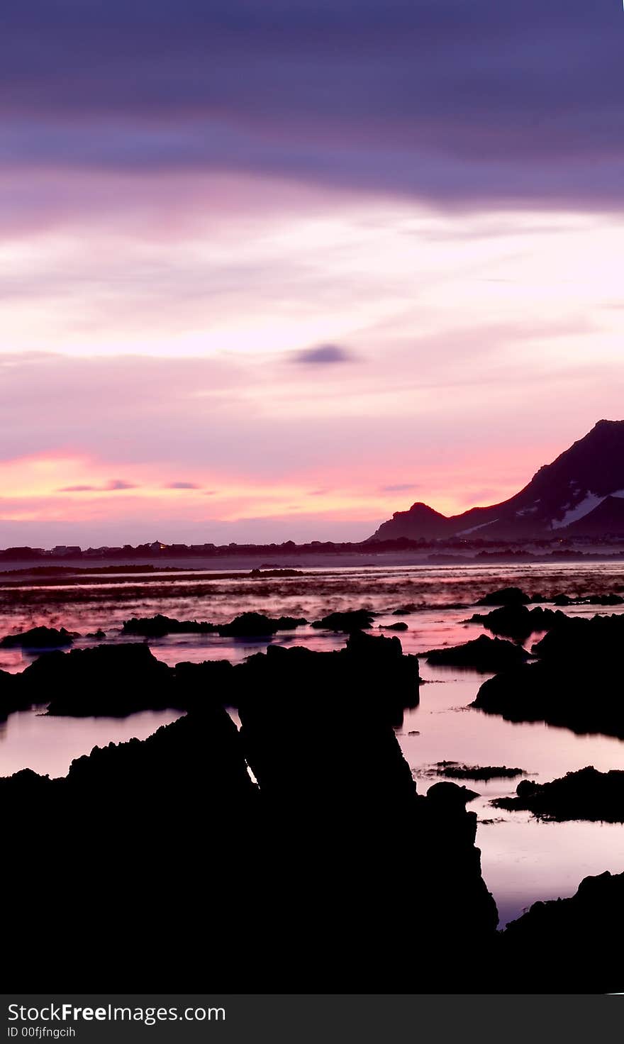 Landscape of an ocean at sunset with blue, pink and purple colors of the sky and rocks sticking out of the water in Bettys Bay, South Africa. Landscape of an ocean at sunset with blue, pink and purple colors of the sky and rocks sticking out of the water in Bettys Bay, South Africa.