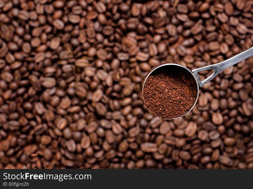 Spoon with grinded coffee (focus on it) over coffee seeds. Spoon with grinded coffee (focus on it) over coffee seeds.