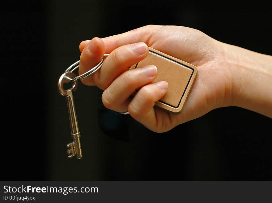 Outstretched hand holding a house key on an isolated black background. Outstretched hand holding a house key on an isolated black background