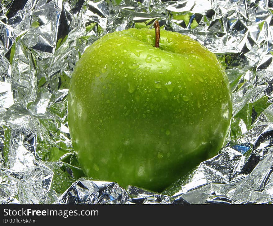 Green apple with drops on a metal, brilliant background.