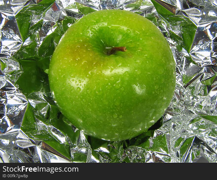 Green apple with drops on a metal, brilliant background.