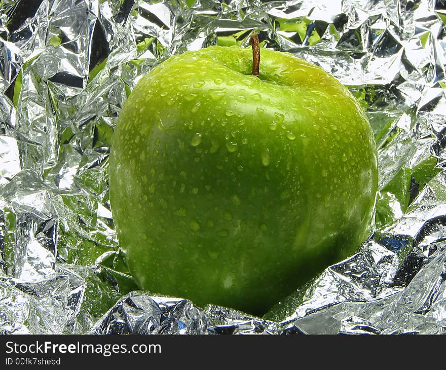 Green apple with drops on a metal, brilliant background.