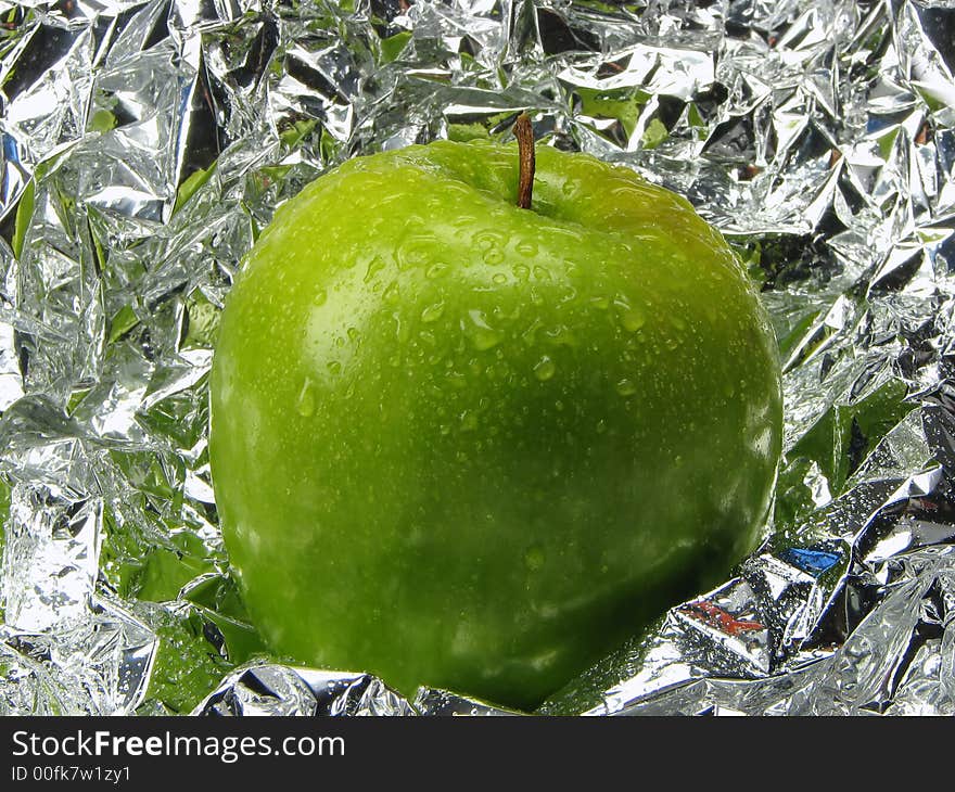 Green apple with drops on a metal, brilliant background.