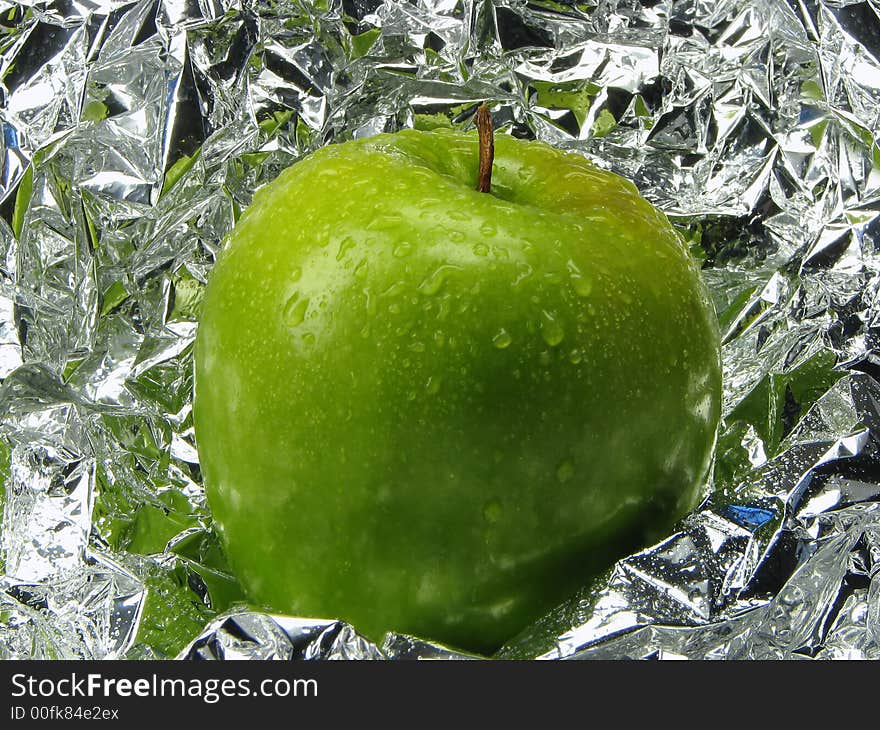 Green apple with drops on a metal, brilliant background.