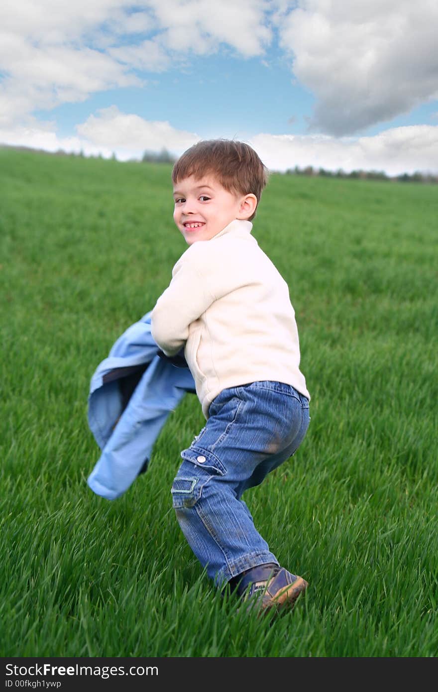 The cheerful boy on a background of a green grass and the sky