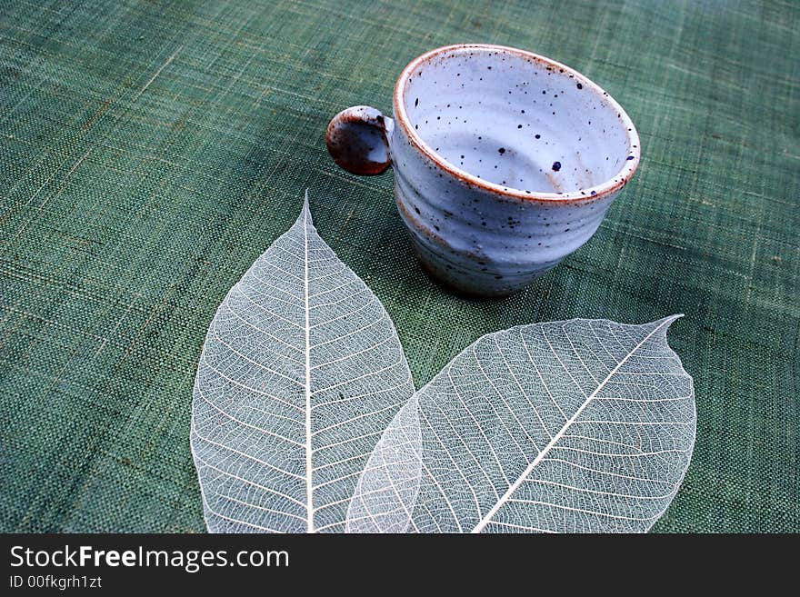 Pottery cup and pretty spring leaves on a green background. Pottery cup and pretty spring leaves on a green background