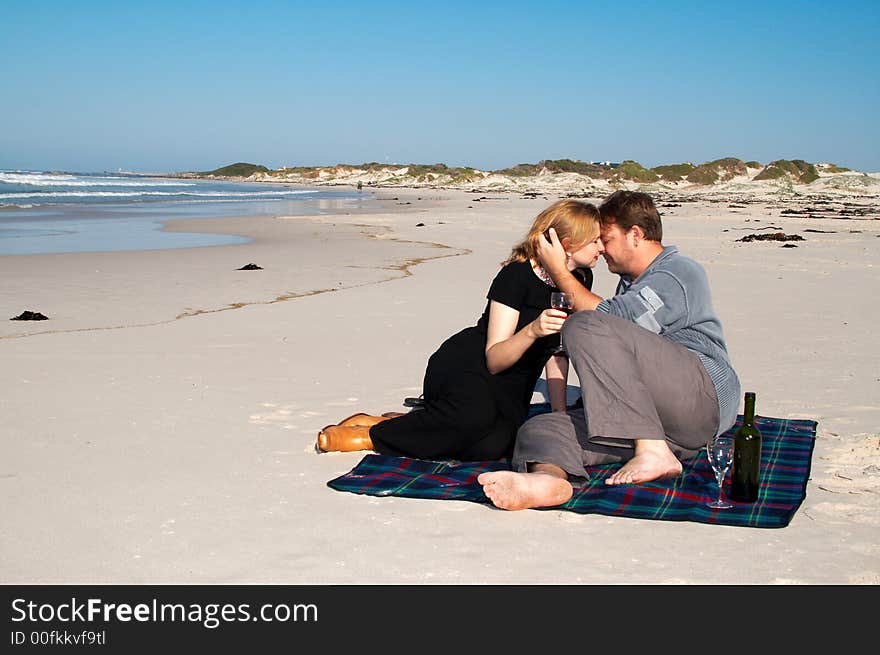 Young married couple moving closer to each other for a kiss. They are enjoying their winter vacation on the beach in South Africa. Shot on a sunny day with blue skies and ocean full of waves in the background. Young married couple moving closer to each other for a kiss. They are enjoying their winter vacation on the beach in South Africa. Shot on a sunny day with blue skies and ocean full of waves in the background.