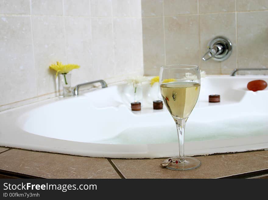 Glass of champagne standing on white bath-tub, decorated with flowers and candles. Glass of champagne standing on white bath-tub, decorated with flowers and candles.