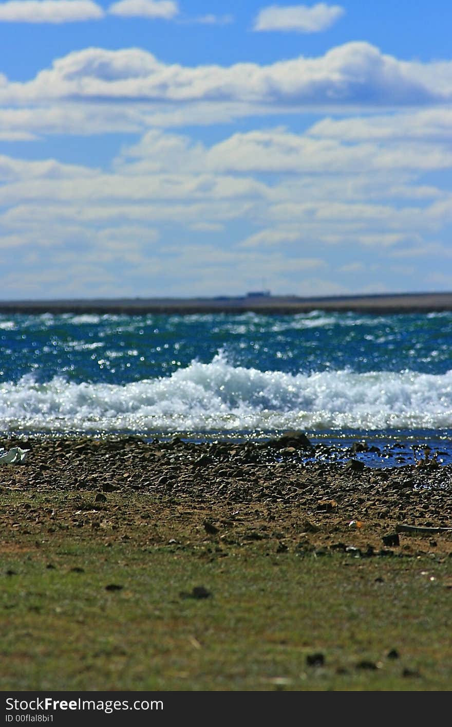 A dam, grass, rocks and stones; water; waves; swells; wall and sky on a windy day. A dam, grass, rocks and stones; water; waves; swells; wall and sky on a windy day