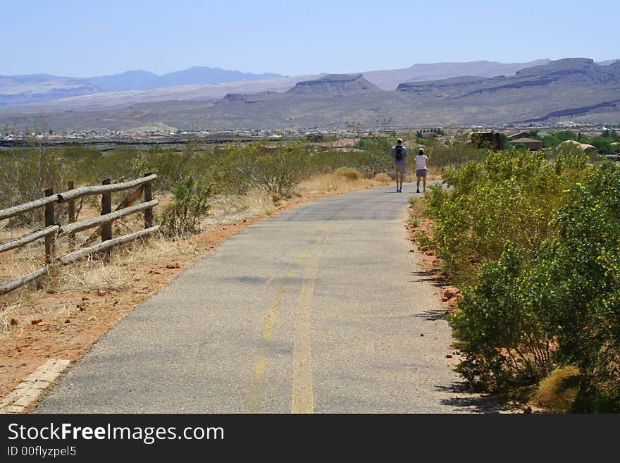 Couple walking down a hiking trail toward town.
Mountains on the horizon. Clear blue sky. Couple walking down a hiking trail toward town.
Mountains on the horizon. Clear blue sky.