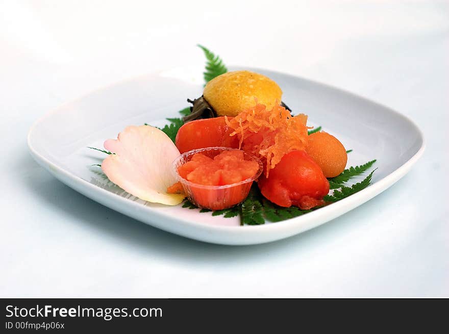 Plate of an orange-colored egg-based Asian dessert with a fern leave and a rose petal on a white plate