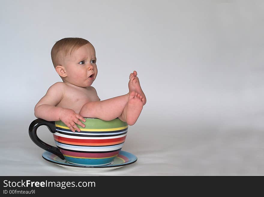 Image of an adorable baby sitting in a colorful, over-sized teacup. Image of an adorable baby sitting in a colorful, over-sized teacup