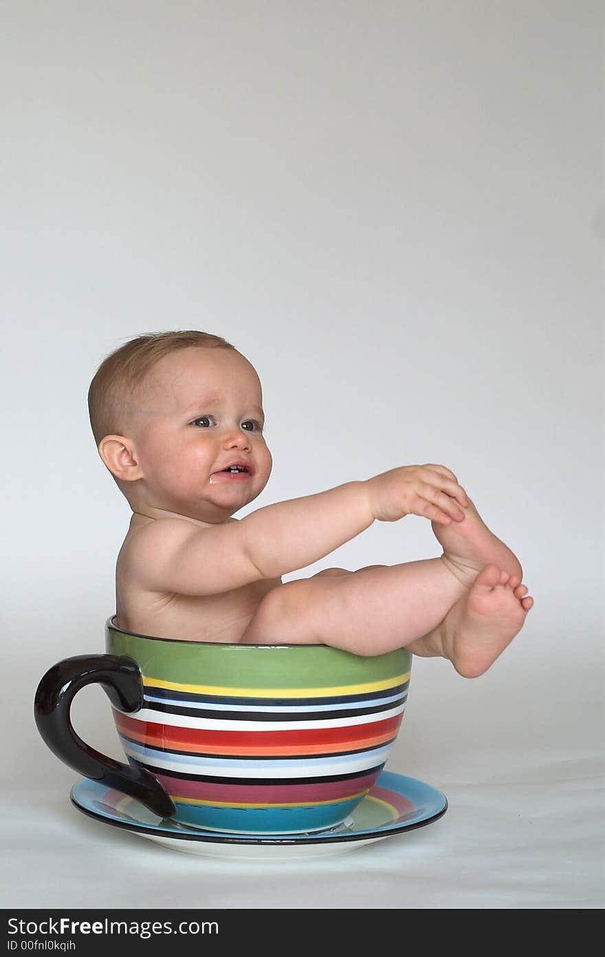 Image of an adorable baby sitting in a colorful, over-sized teacup. Image of an adorable baby sitting in a colorful, over-sized teacup