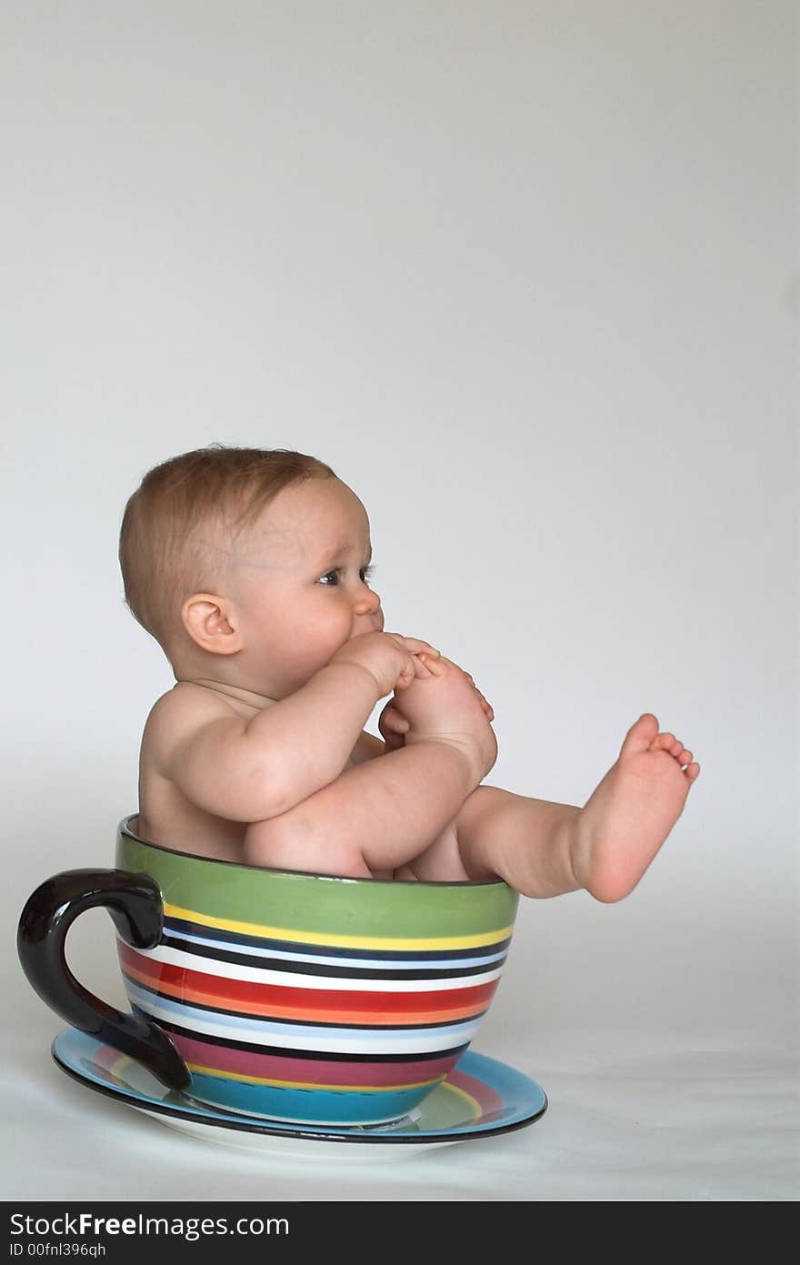 Image of an adorable baby sitting in a colorful, over-sized teacup. Image of an adorable baby sitting in a colorful, over-sized teacup