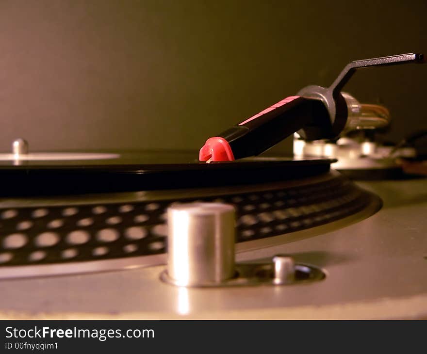 Photo of dj turntable needle on record with the focus on the needle illuminated under party lights.