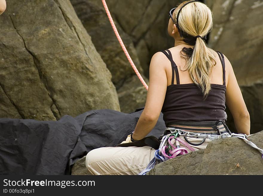 A rock climber woman seating and looking up at a cliff