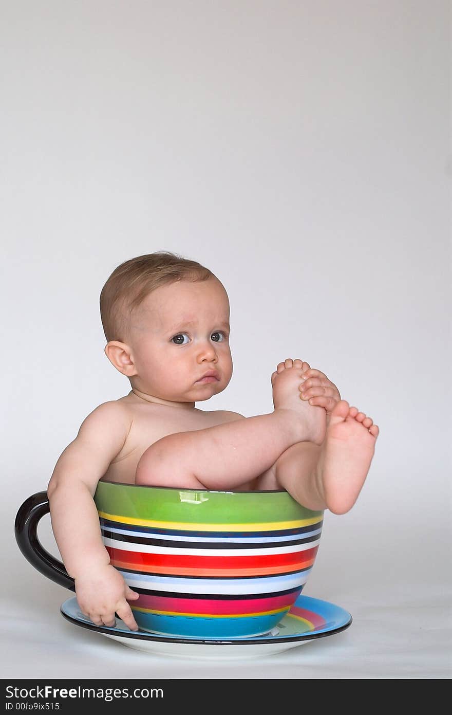 Image of an adorable baby sitting in a colorful, over-sized teacup. Image of an adorable baby sitting in a colorful, over-sized teacup