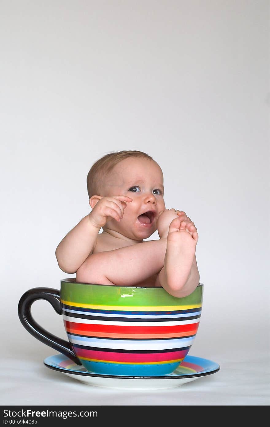 Image of an adorable baby sitting in a colorful, over-sized teacup. Image of an adorable baby sitting in a colorful, over-sized teacup