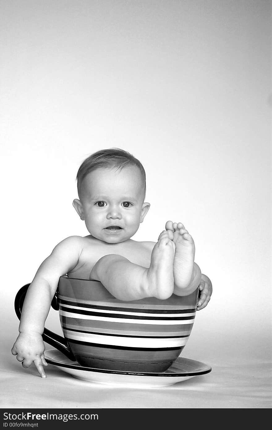 Black and white image of cute baby sitting in an over-sized teacup. Black and white image of cute baby sitting in an over-sized teacup