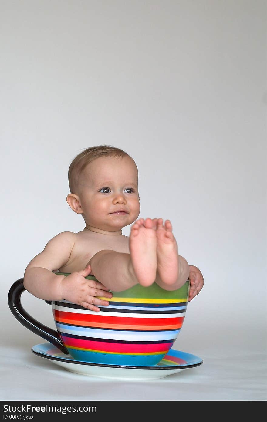 Image of an adorable baby sitting in a colorful, over-sized teacup. Image of an adorable baby sitting in a colorful, over-sized teacup