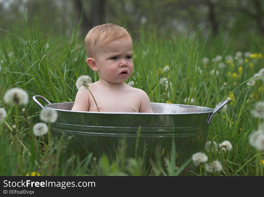 Image of a cute baby sitting in a galvanized tub in a meadow. Image of a cute baby sitting in a galvanized tub in a meadow