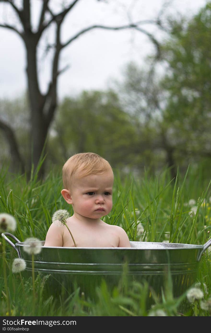 Image of a cute baby sitting in a galvanized tub in a meadow. Image of a cute baby sitting in a galvanized tub in a meadow