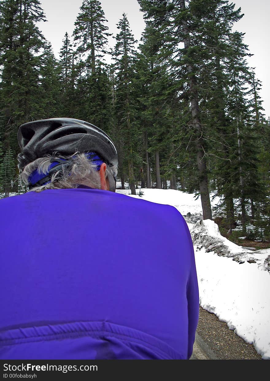 Road cyclist in purple on mountain road in snow. Road cyclist in purple on mountain road in snow