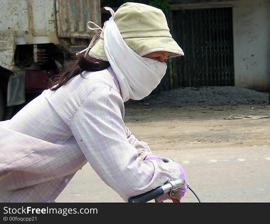 Lady riding bike, covered up from sun and pollution in Vietnam