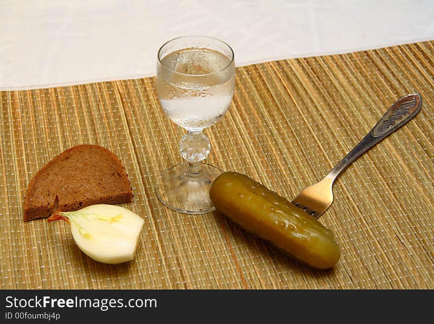 Wineglass of vodka and tradional russian snacks for it - onion, brown bread and sour cucumber. Wineglass of vodka and tradional russian snacks for it - onion, brown bread and sour cucumber