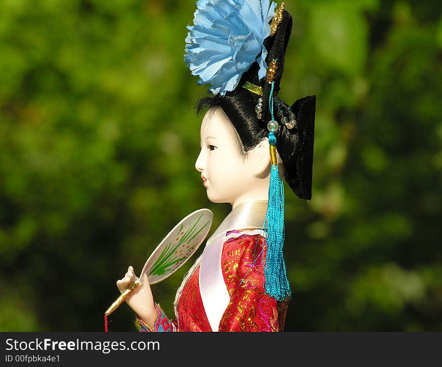 A Geisha doll with green foliage in the background. A Geisha doll with green foliage in the background.