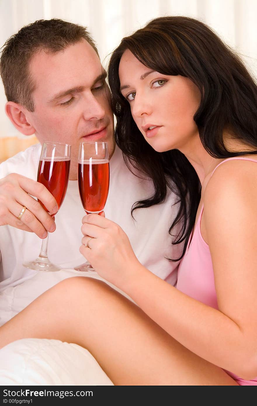 Beautiful couple in bed drinking wine.