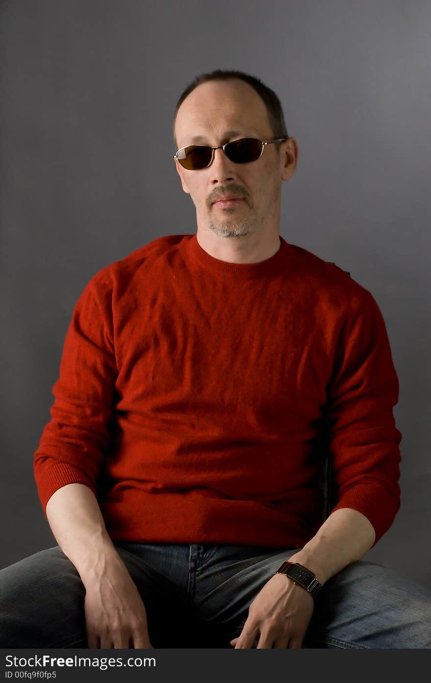 The man in a red sweater and glasses sits on a chair. The man in a red sweater and glasses sits on a chair