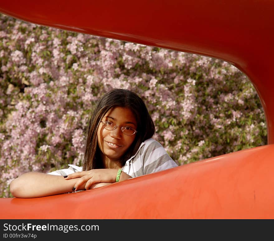 Portrait of an attractive young teen framed by a large orange sculpture and on a backdrop of lush spring blossoms. Portrait of an attractive young teen framed by a large orange sculpture and on a backdrop of lush spring blossoms.