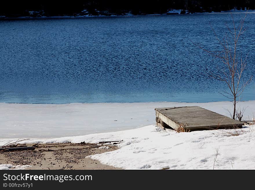 A gray dock juts diagonally into a pristine, half-frozen lake in Miners Bay. A gray dock juts diagonally into a pristine, half-frozen lake in Miners Bay