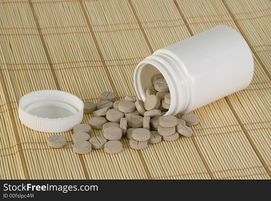 A blank plastic bottle with vitamin supplements spilling out.