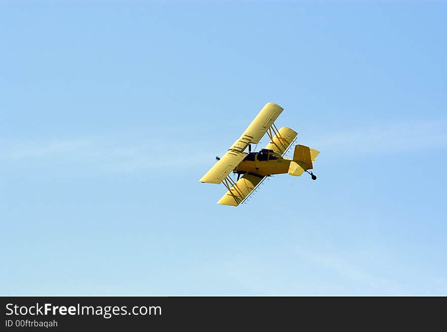 A yellow biplane crop duster preparing to make a pass over a field.