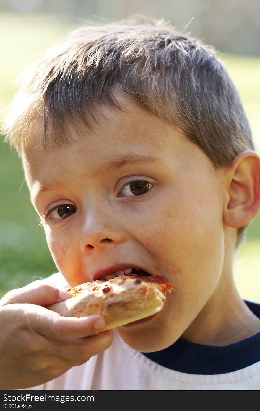 Cute young boy eating pizza outside