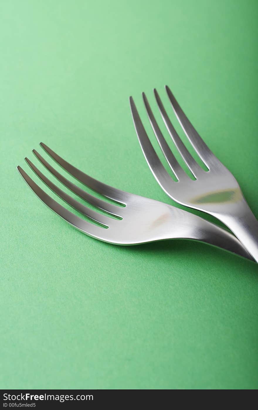 Two forks head on green paper background, shallow DOF