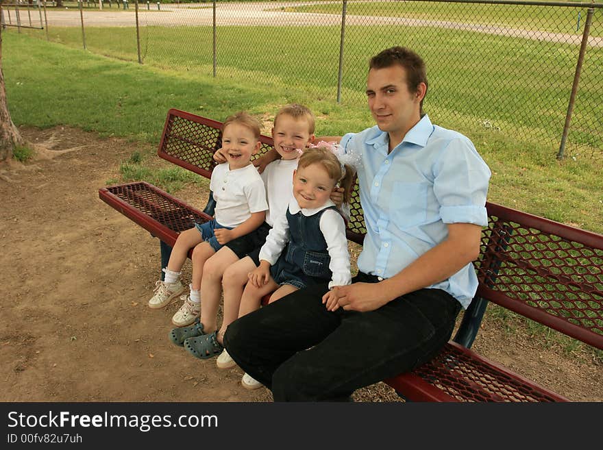 Father, son, and twin daughters sitting on a bench at the playground. Father, son, and twin daughters sitting on a bench at the playground