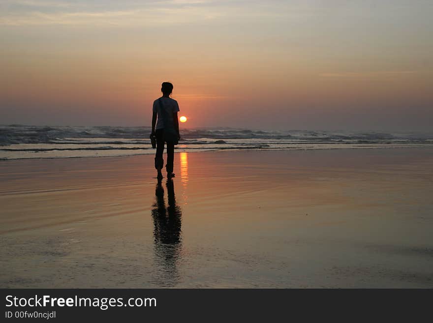 The girl who standing alone in the beach sunset and has reflection in the water. The girl who standing alone in the beach sunset and has reflection in the water