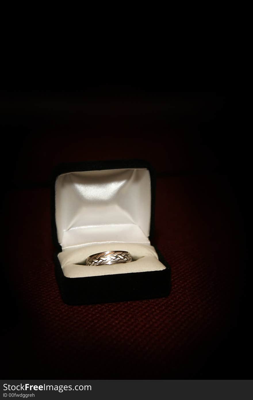 Wedding ring in a ring box on a red textured surface with a spotlight effect. Wedding ring in a ring box on a red textured surface with a spotlight effect