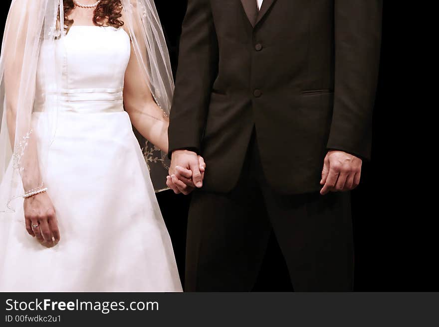 Bride and groom holding hands during their wedding ceremony with bride's engagement ring showing