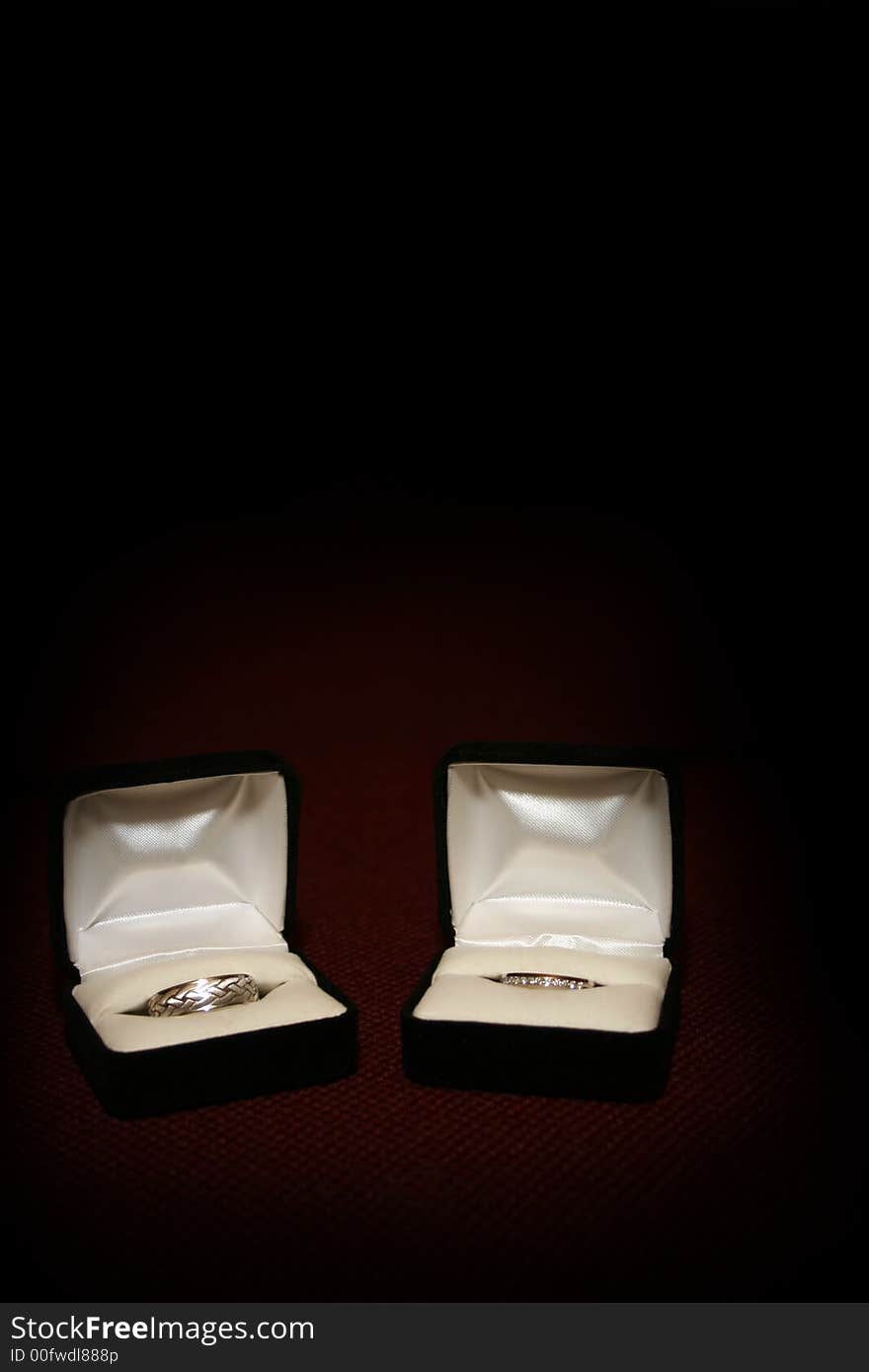 Two ring boxes with wedding rings displayed, on a red textured surface with dark background