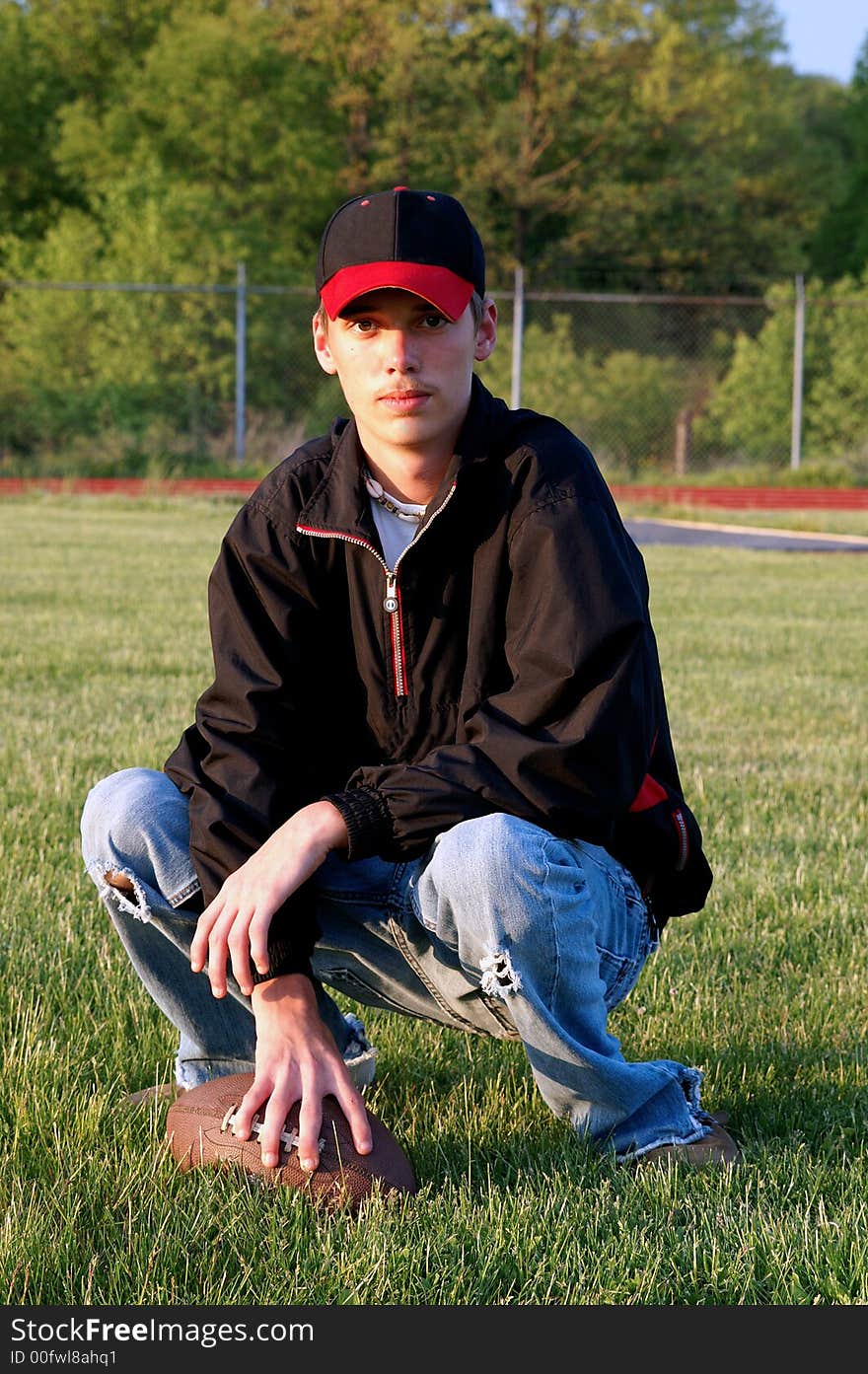 A handsome young boy kneeling on a football field with his football. A handsome young boy kneeling on a football field with his football